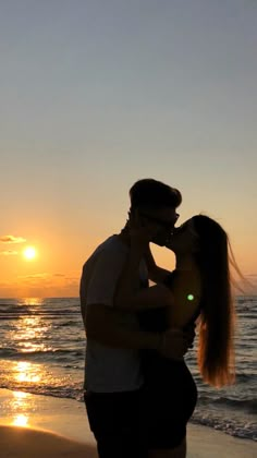 a man and woman kissing on the beach at sunset