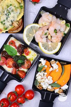 four trays filled with different types of food on top of a white tablecloth