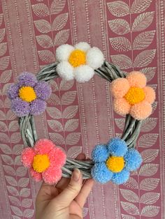 a hand holding a yarn wreath with flowers on it