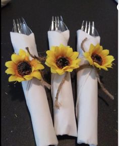 four forks with sunflowers tied to them on a black tableclothed surface