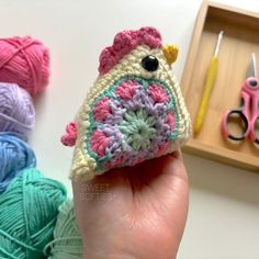 a hand holding a small crocheted object in front of some yarn and scissors