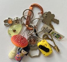 there are many different key chains on this white surface, including one with a mushroom