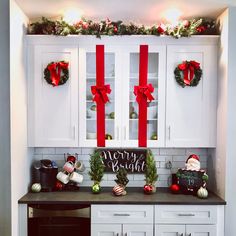 a kitchen with white cabinets and christmas decorations on the counter top, along with red bows