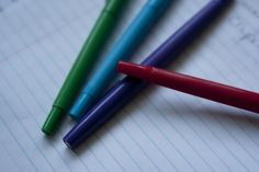 three different colored pens sitting on top of lined paper