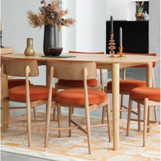 a dining table with orange chairs and a vase filled with flowers on top of it