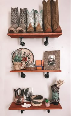 two wooden shelves with cowboy boots and other items on them, along with plates and vases