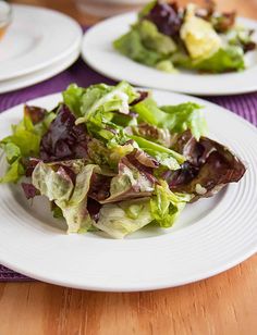 two white plates filled with salad on top of a wooden table