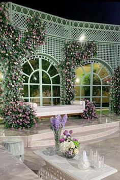 a white bench sitting in the middle of a room filled with flowers and greenery