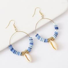 a pair of blue and white beaded hoop earrings with seashells on them