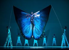 a group of people standing on stilts in front of a blue butterfly