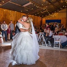 a bride and groom dance together at their wedding reception in the barn with guests watching