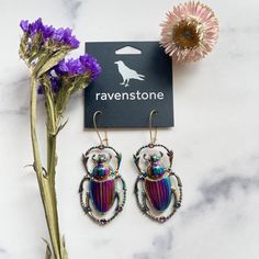 a pair of earrings sitting next to a purple flower