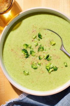 a bowl of broccoli soup with a spoon in it on a wooden table