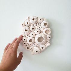 a hand is pointing at a white wall decoration with holes in the shape of balls