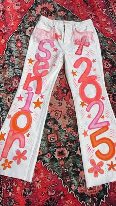 white pants with pink and orange lettering on them sitting on a rug in front of a red carpet