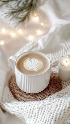 a cup of cappuccino sitting on top of a white blanket next to a lit candle