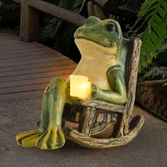 a frog statue sitting on top of a wooden bench next to a lit candle holder