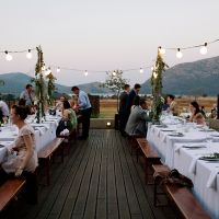 a group of people sitting at tables with white tablecloths and lights strung over them