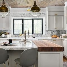 a large kitchen with white cabinets and marble counter tops, along with two bar stools