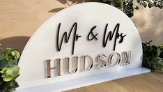 a white sign that reads mr and mrs hudson on it's side next to some plants