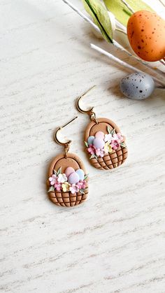 Step into the season with style and charm with these delightful floral Easter basket dangle earrings, meticulously crafted from quality polymer clay. Each pair features an Easter basket overflowing with colorful eggs and flowers. The charm hangs from a nickel safe, lead and cadmium free 18k gold plated brass post making safe for sensitive ears.   These earrings are lightweight and comfortable to wear all day. They would make a great addition to your jewelry collection or a thoughtful gift for so Easter Clay Earrings, Easter Egg Earrings, Egg Earrings, Polymer Clay Gifts, Clay Pendants, Easter Egg Basket, Easter Jewelry, Unique Products Design, Spring Earrings