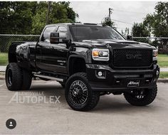 a black truck parked in a parking lot next to a chain link fence and trees