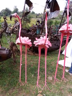 pink flamingos are standing in the grass near boats and other junkyards that have been turned into art