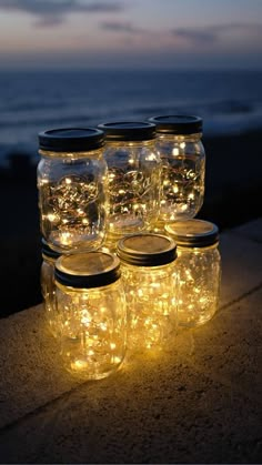 mason jars with fairy lights in them sitting on a ledge by the ocean at night