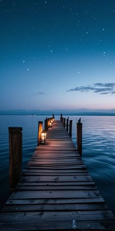 a wooden dock with lights on it at night over the water and stars in the sky