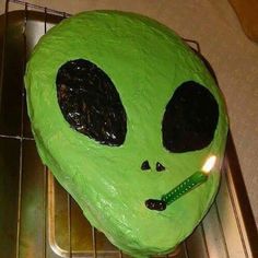 a green cake with a lit candle in it's mouth on a cooling rack