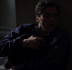 a man sitting down in the dark with his arm around his neck and looking at something