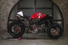 a red and white motorcycle parked in front of a brick wall with an arched window