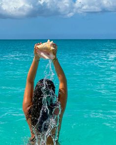 a woman standing in the ocean with her arms up above her head holding a shell