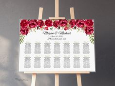 a wedding seating chart with red flowers and greenery on an easel against a gray wall