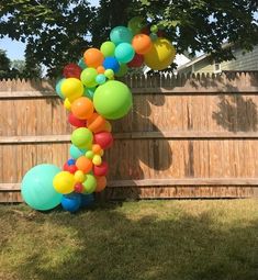 a number one made out of balloons sitting in the grass next to a wooden fence