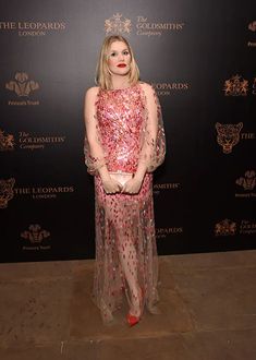 a woman standing in front of a black wall wearing a red and white dress with sequins on it