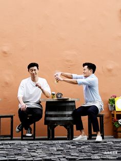 two men are sitting at a table and one is holding a beer in his hand