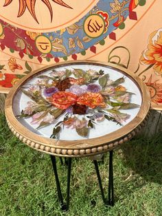 a table with flowers on it sitting in the grass next to a large painting and an umbrella