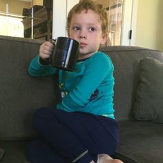 a little boy sitting on top of a couch holding a coffee cup in his hand