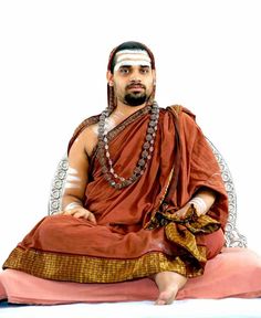 a man sitting on top of a white chair wearing a red and gold outfit with chains around his neck