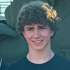 a young man with curly hair smiling at the camera while standing in front of a statue