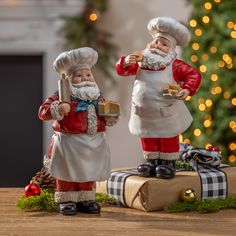 two santa clause figurines standing next to each other on a table near a christmas tree