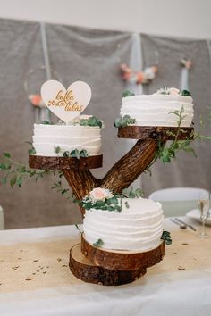 two tiered wedding cake sitting on top of a wooden tree slice with greenery