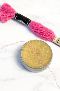 a pink and yellow thread is next to a small round object on a white surface