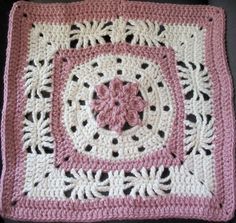 a pink and white crocheted square with a flower on the center is sitting on a black surface