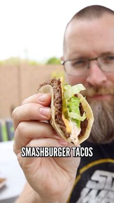 a man holding up a taco in front of his face with the caption, smashburger tacos