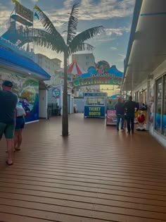 people are walking on the boardwalk at an amusement park with palm trees and carnival rides