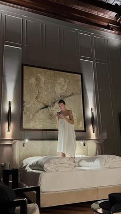 a man standing on top of a bed in a bedroom next to a large painting