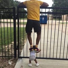 a man standing on top of a child's head in front of a fence