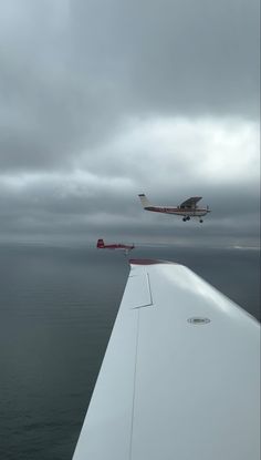 an airplane flying over the ocean on a cloudy day with another plane in the background